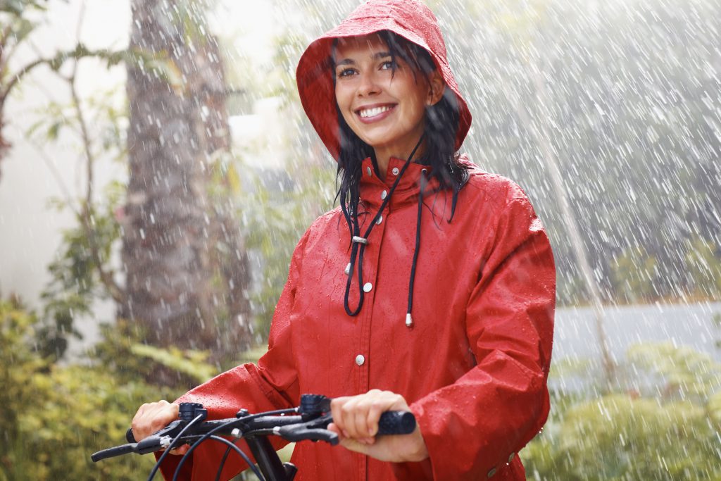 Portrait of young woman in red raincoat on bike in rain